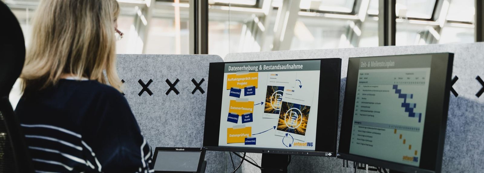 Zwei Bildschirme in einem Besprechungsraum zeigen Auswertungsfolien – links eine Übersicht zur Datenerhebung und Bestandsaufnahme, rechts einen Balkenplan; davor eine Person im Gespräch.
