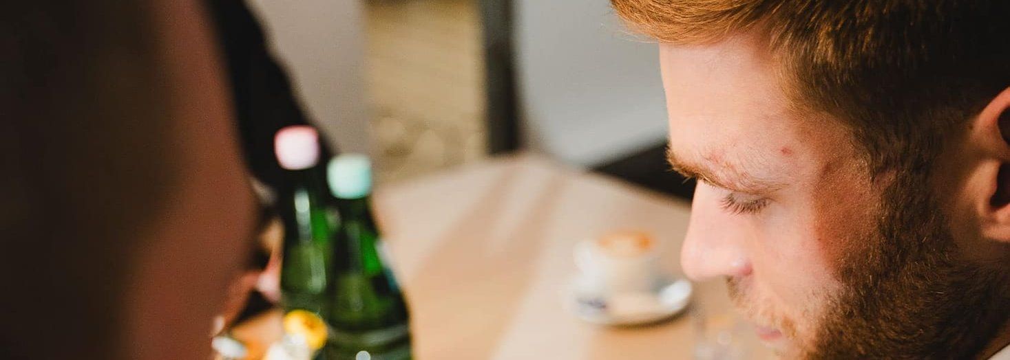 Über die Schulter fotografiert: Ein Mann im Sakko macht sich an einem Besprechungstisch Notizen auf einem Blatt Papier, daneben Getränke und Kaffee.