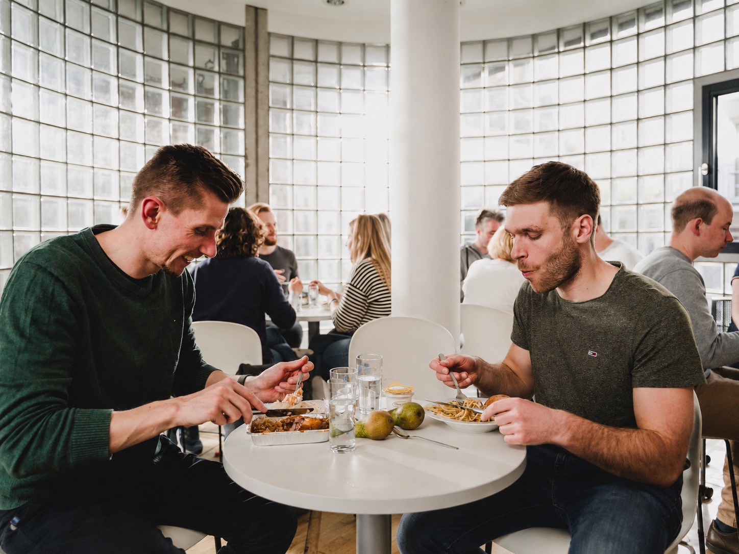 Zwei Kollegen beim gemeinsamen Mittagessen in einem hellen Aufenthaltsraum.